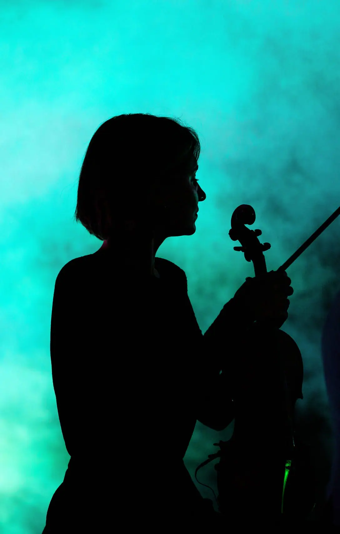 Siluetă de violonistă pe fundal turcoaz cu fum