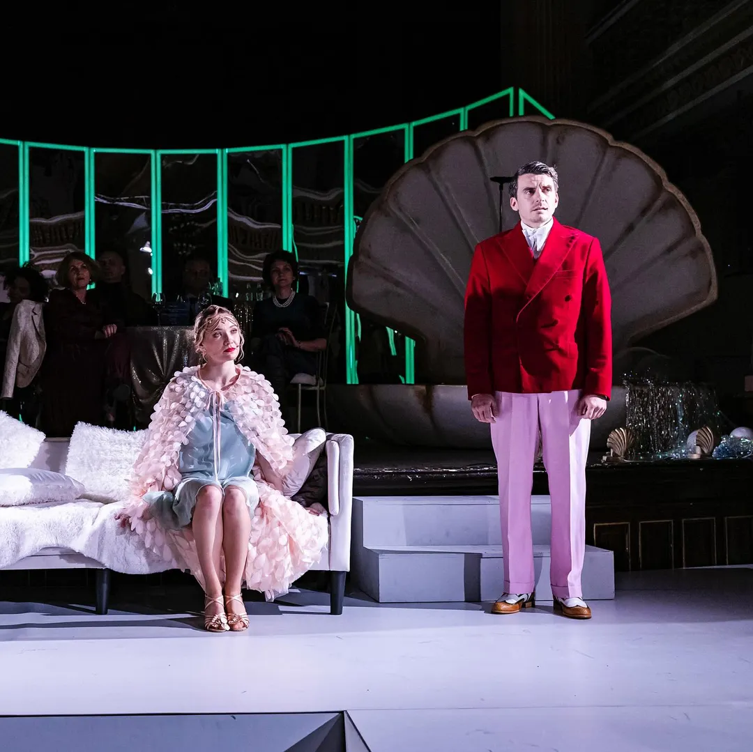 Două personaje pe scena imersivă din Marele Gatsby, în fața unui decor verde