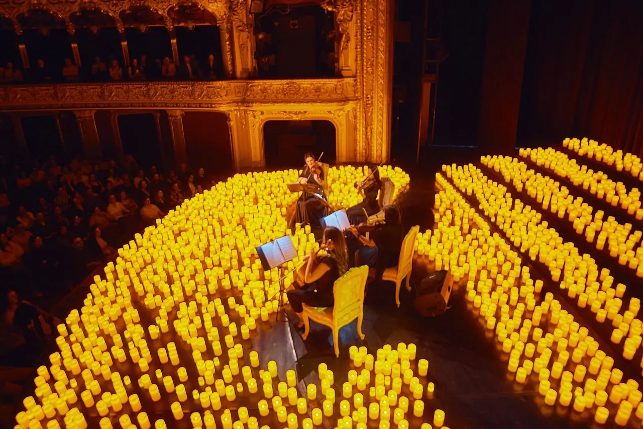 Sală de teatru cu scena și stalurile pline de lumânări, la un concert Multisenzorial